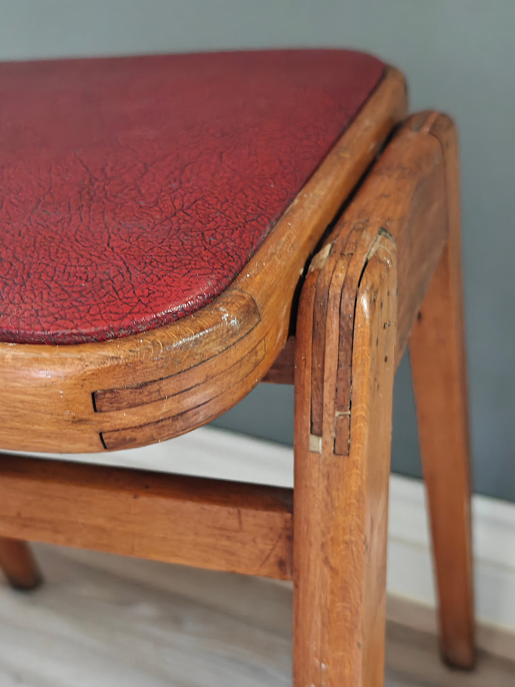 Close-up of mid-century wood frame stool with red vinyl seat