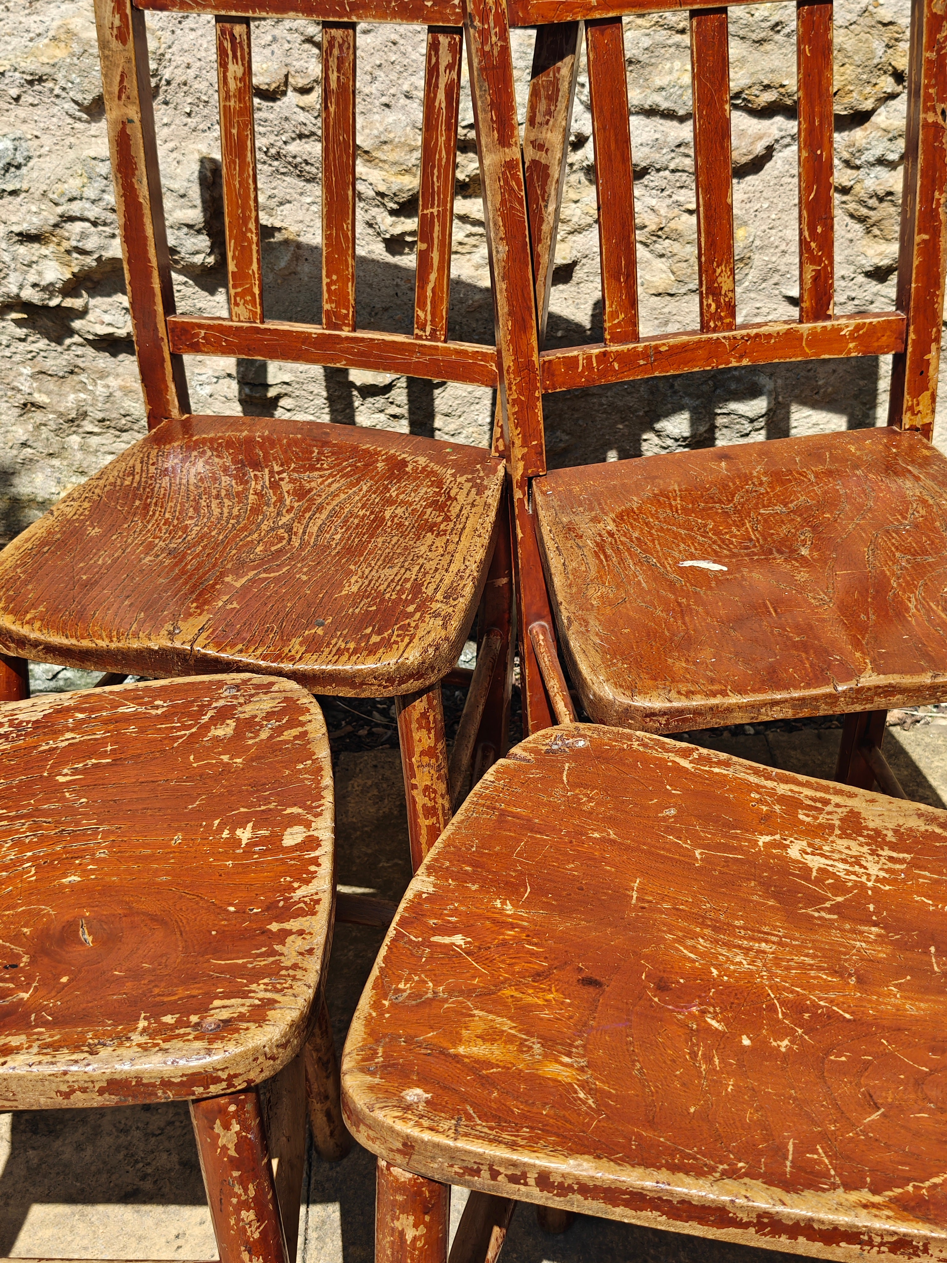 Four weathered wooden dining chairs with distressed reddish-brown painted seats and backs