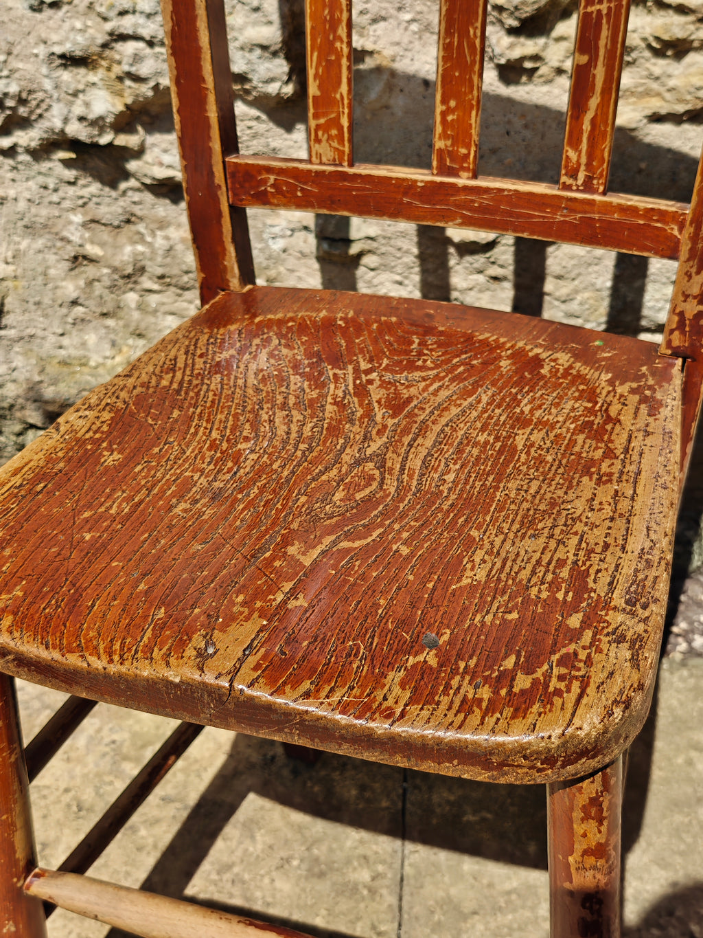 A close-up of a rustic wooden chair with a distressed finish, showing the seat and backrest 