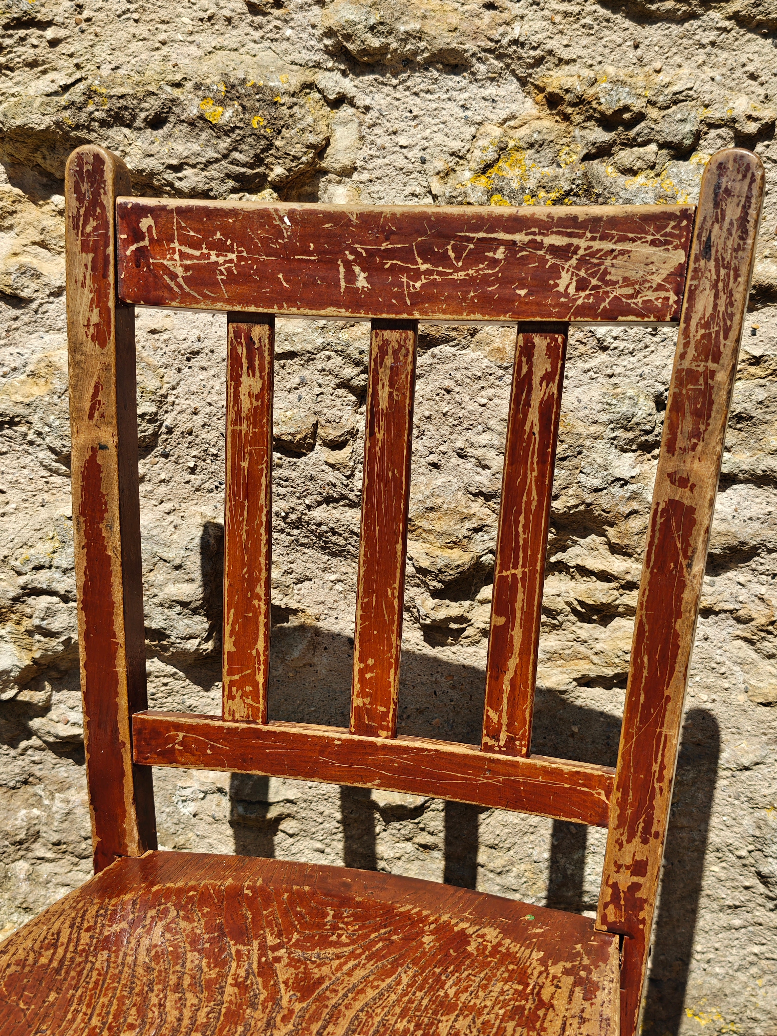 A close-up of the back rest of a rustic wooden chair with a distressed reddish-brown finish