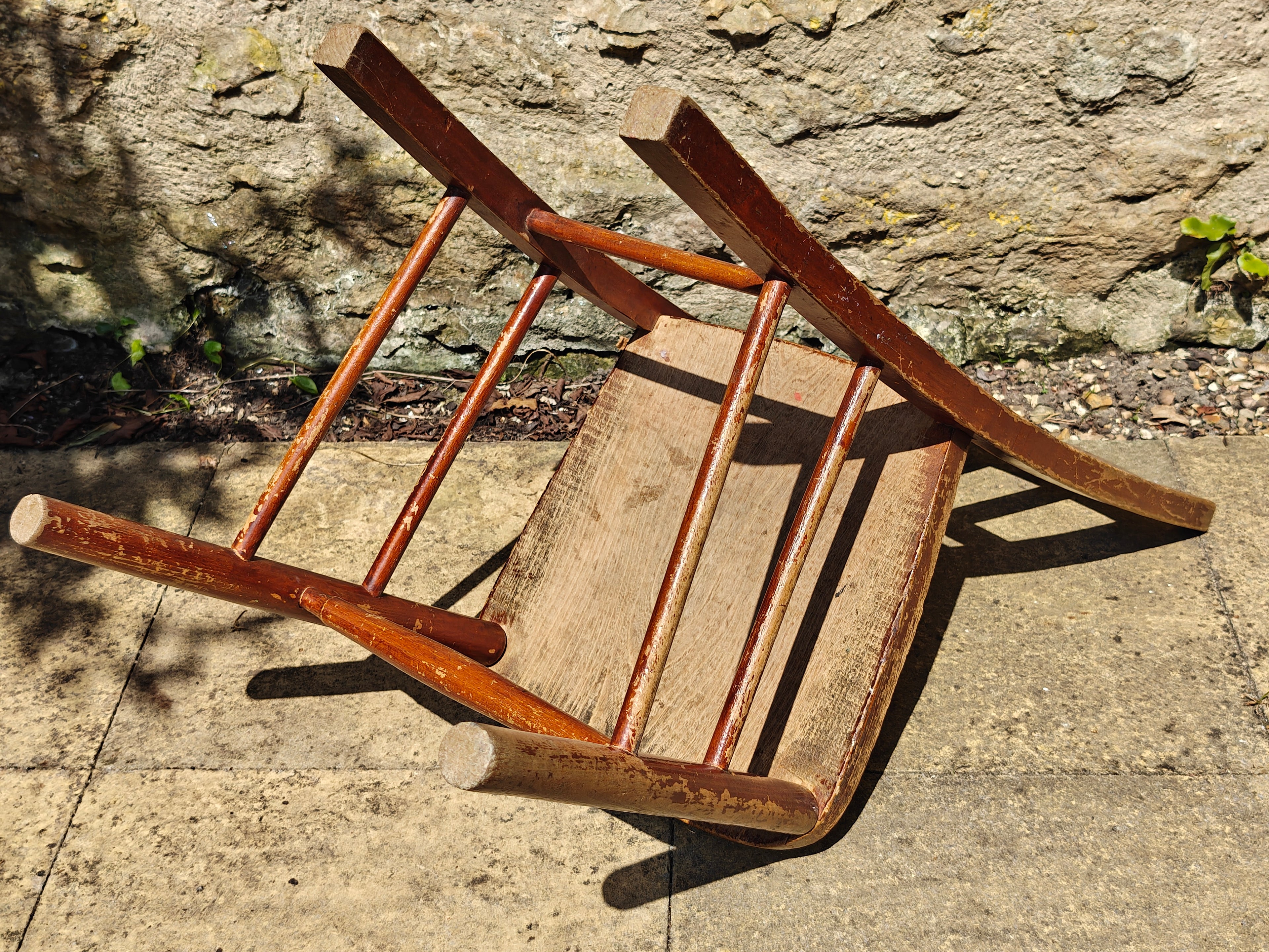 The underside of a rustic wooden chair with a distressed reddish-brown finish