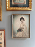 A framed vintage-style portrait print of a woman in a white wedding dress holding flowers.