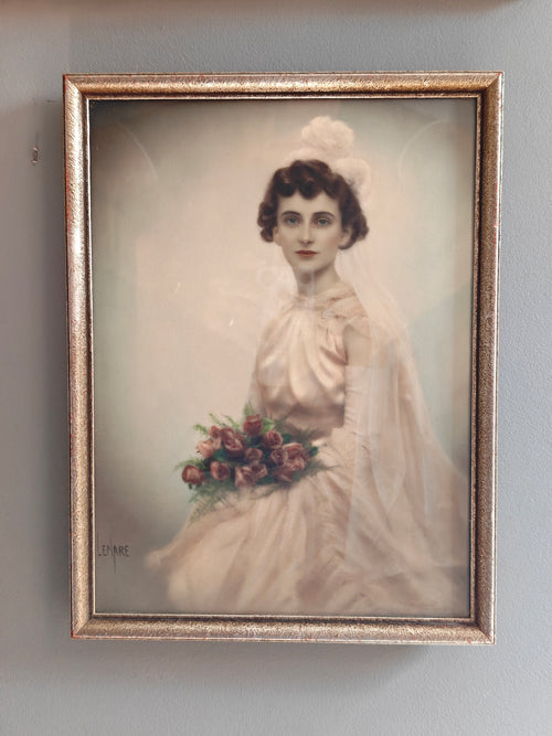 A vintage framed portrait print of a woman in a white bridal gown holding a bouquet of pink and red flowers, set in an ornate gold-toned frame.