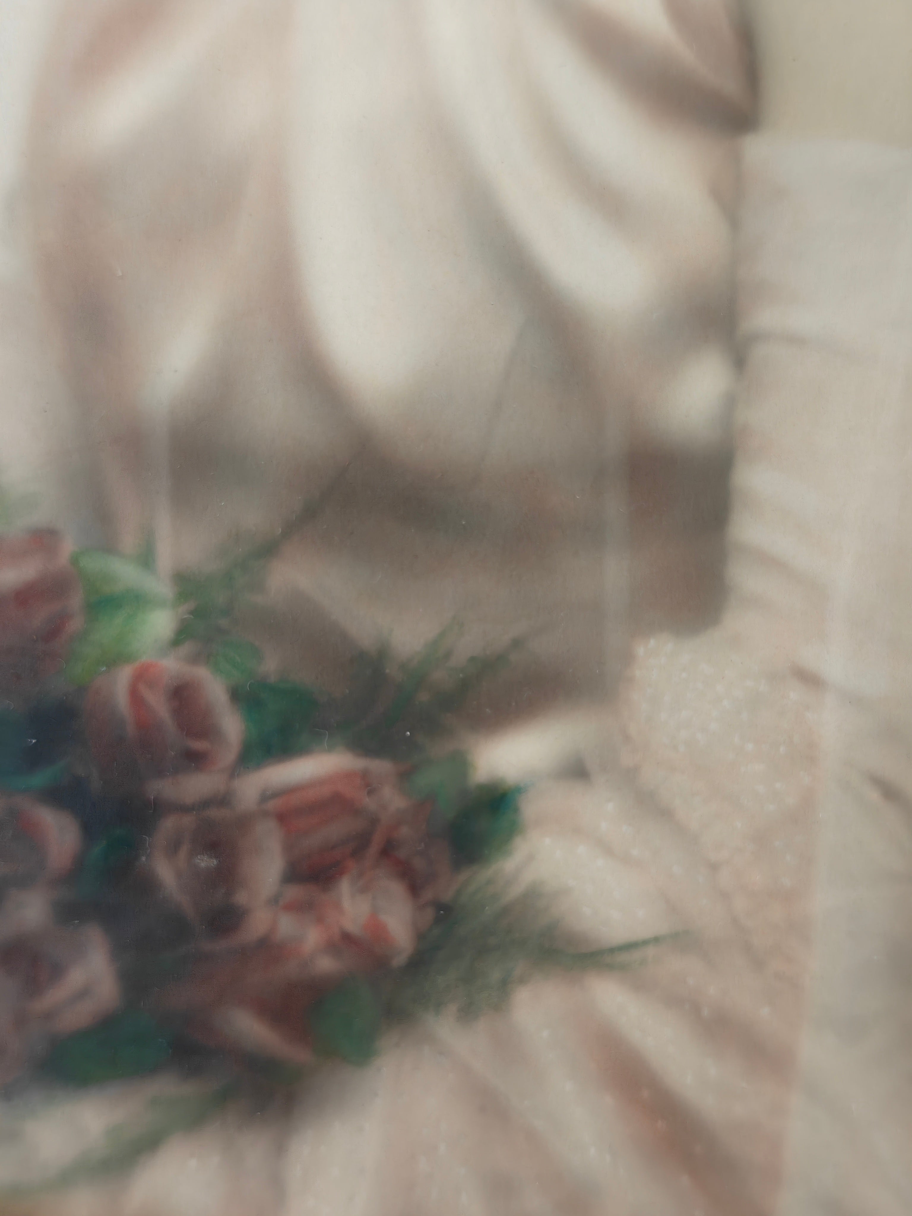 A close-up, soft-focus view of a bouquet of dusty pink roses with green foliage held against a cream-colored satin fabric background.
