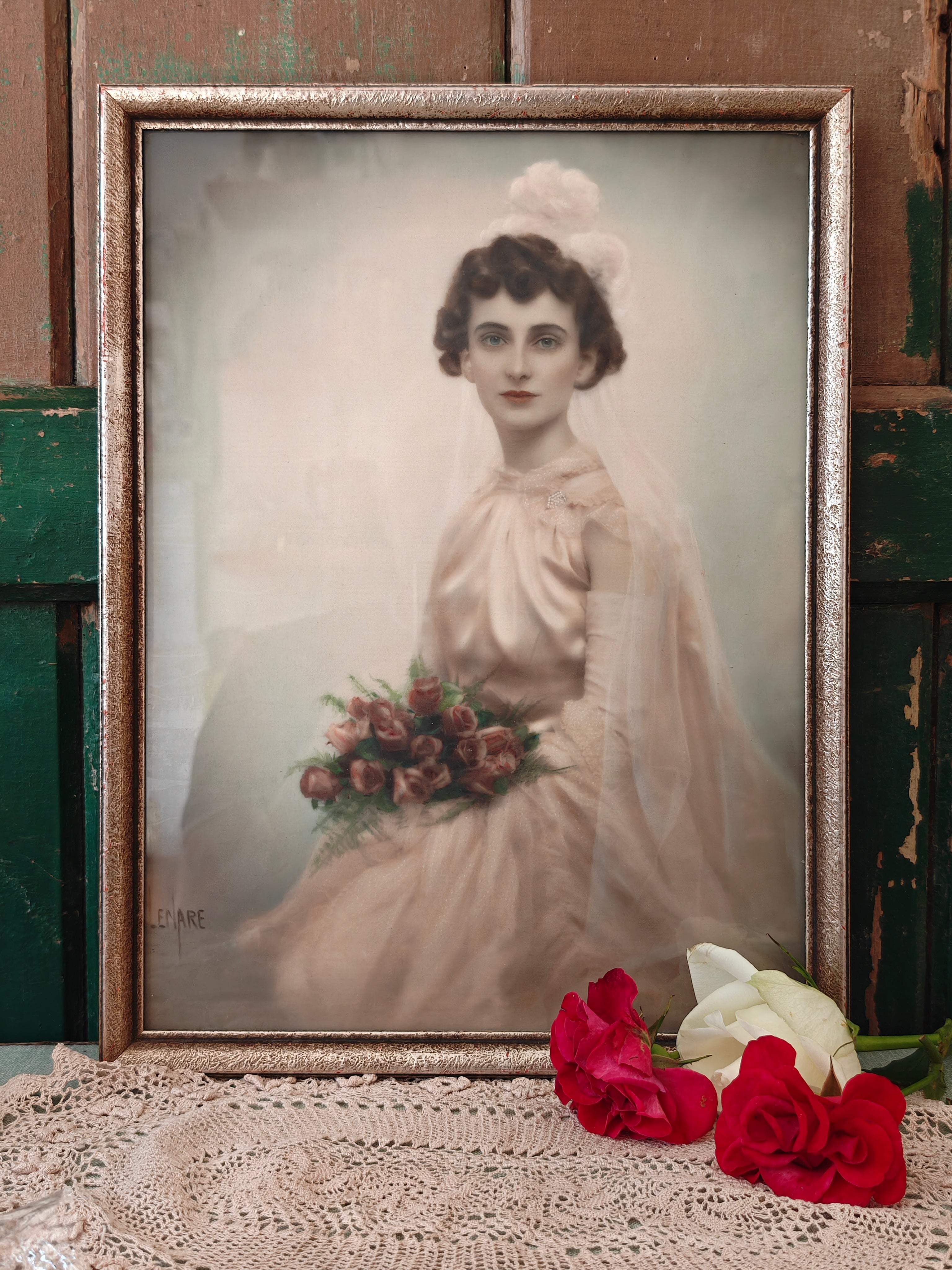 A vintage framed portrait print of a woman in a white bridal gown holding a bouquet of pink and red flowers, set in an ornate gold-toned frame.