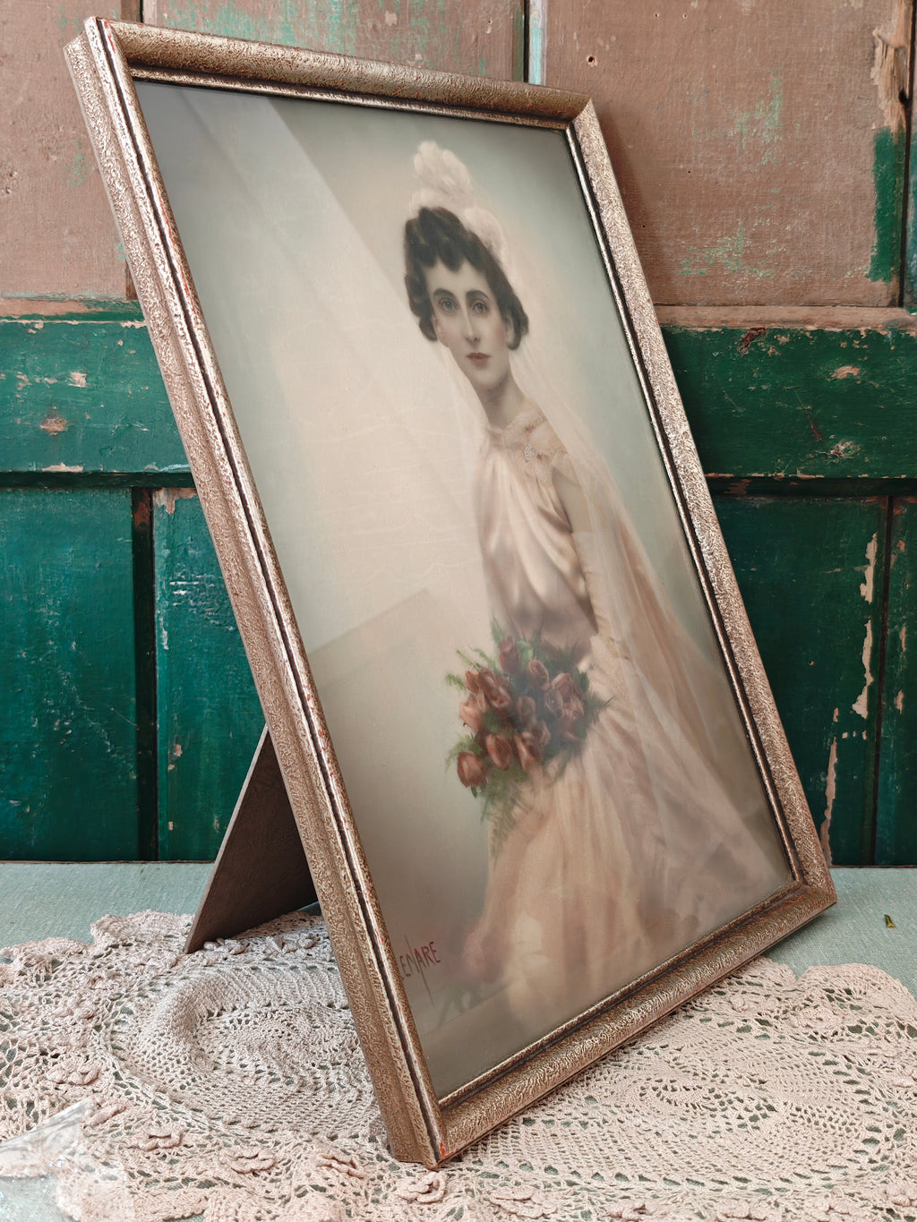 A vintage framed portrait print of a woman in a white bridal gown holding a bouquet of pink and red flowers, set in an ornate gold-toned frame.