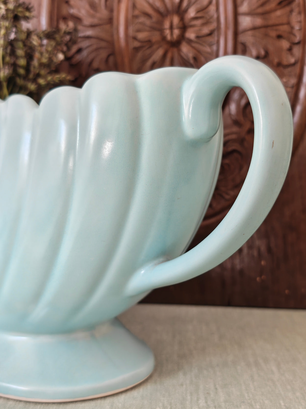 Close up of the handle of a large pale blue mantle vase with fluted form