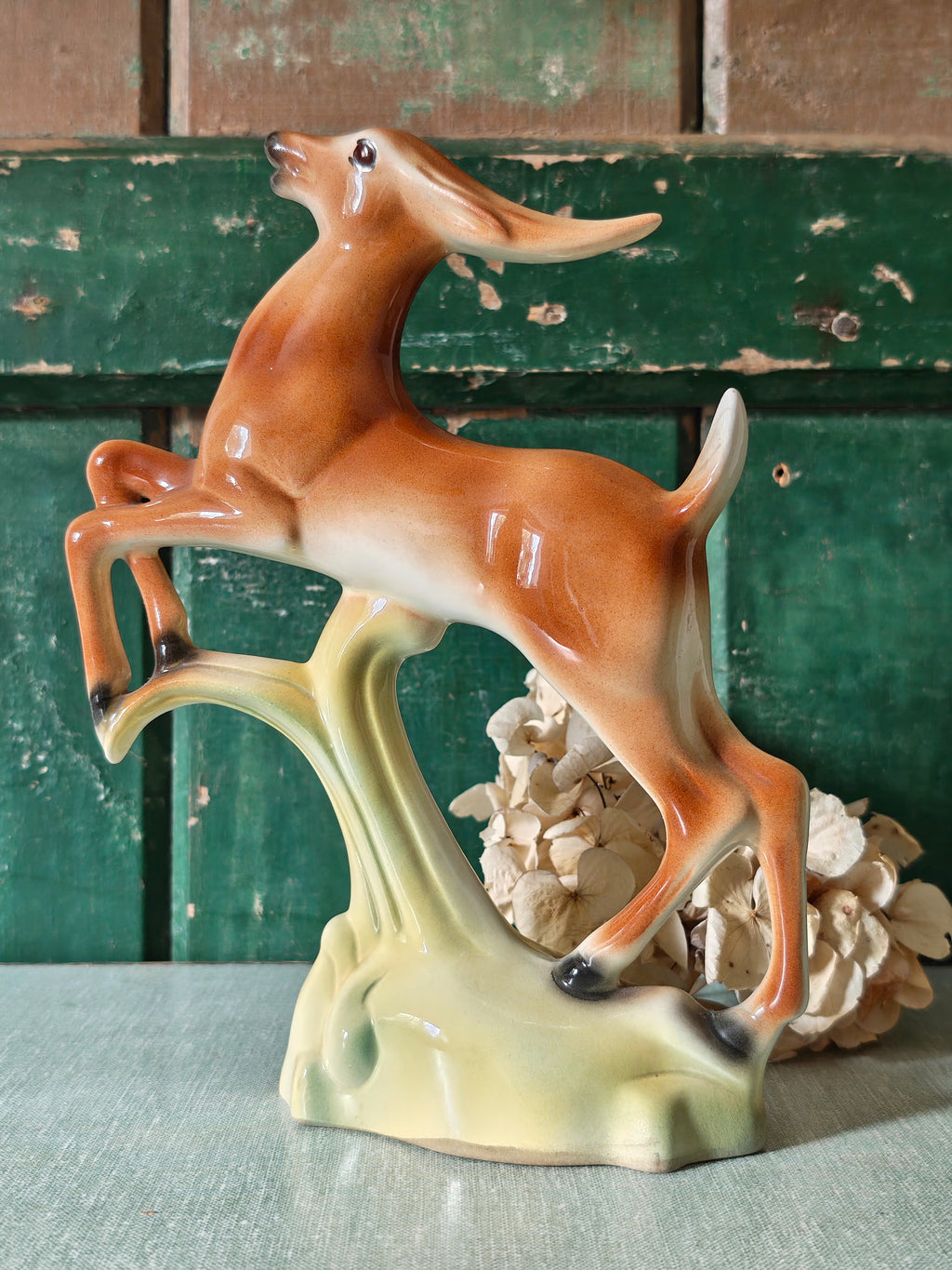 A vintage ceramic deer figurine in a rearing pose, featuring a glossy brown and cream body mounted on a pale green base.