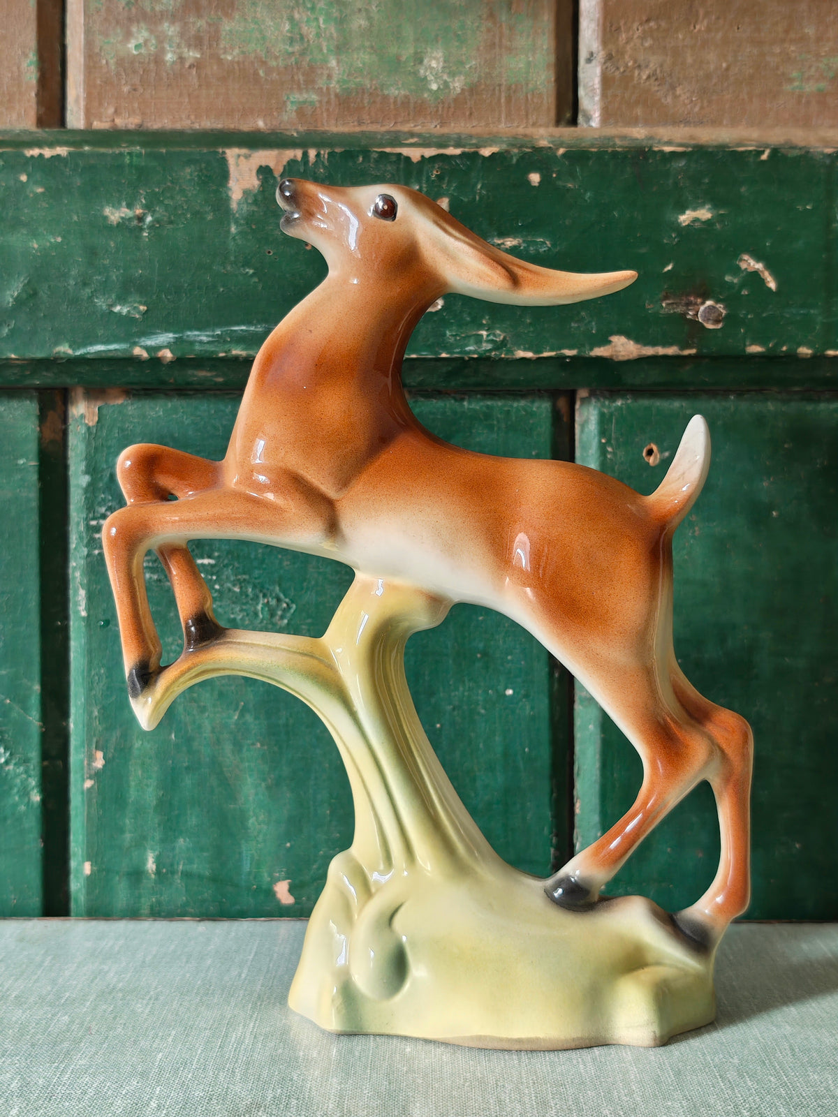 A vintage ceramic deer figurine in a rearing pose, featuring a glossy brown and cream body mounted on a pale green base.
