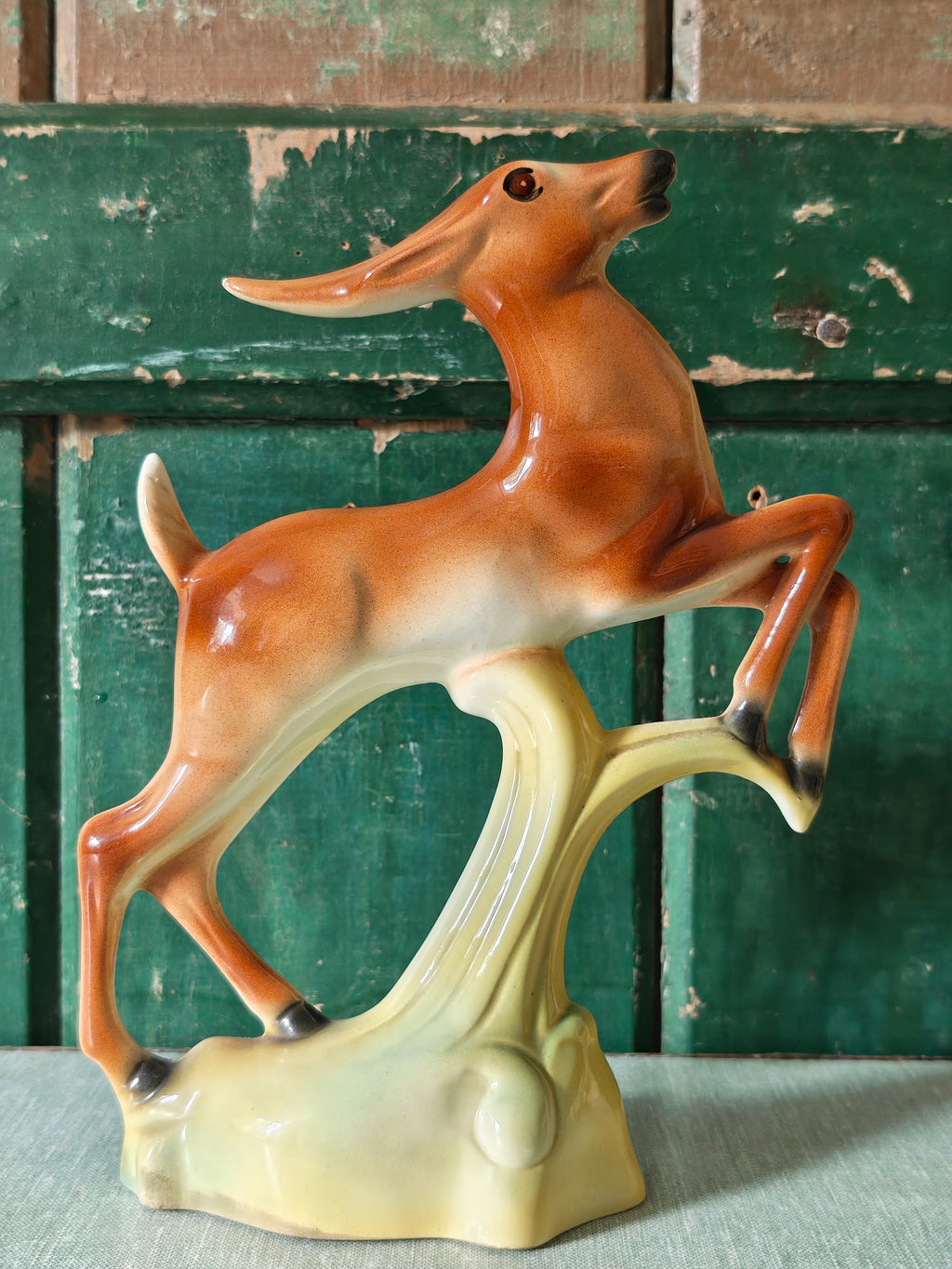 A vintage ceramic deer figurine in a rearing pose, featuring a glossy brown and cream body mounted on a pale green base.