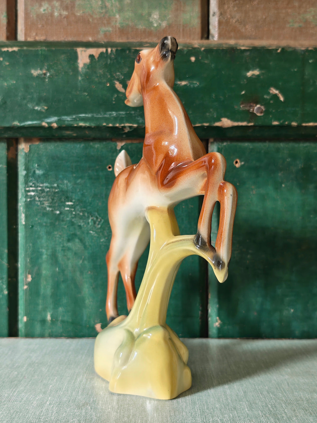A vintage ceramic deer figurine in a rearing pose, featuring a glossy brown and cream body mounted on a pale green base.