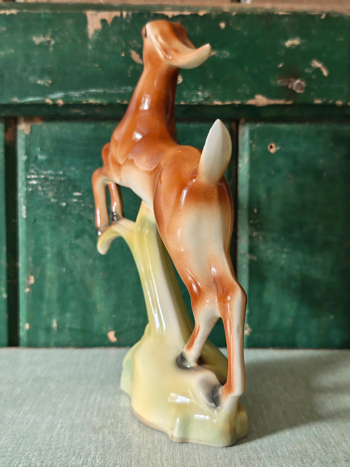 A vintage ceramic deer figurine in a rearing pose, featuring a glossy brown and cream body mounted on a pale green base.
