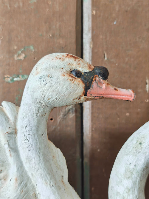 A close-up of a distressed white swan cast iron doorstop figurine with a pink beak and black eye detail.