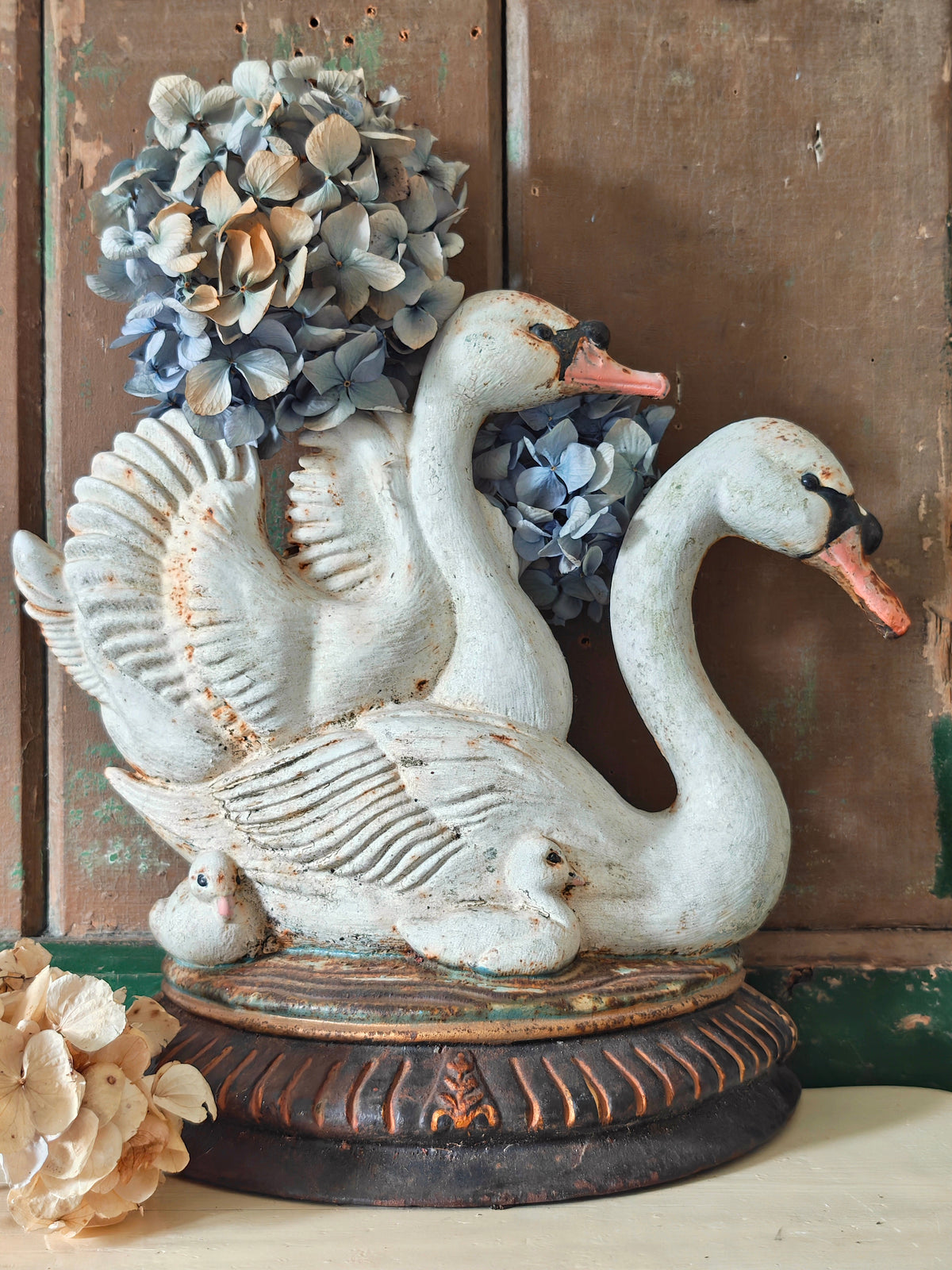 A decorative cast iron doorstop modelled as two swans and cygnets on a round pedestal base. The swans are painted in a distressed off-white finish with orange beaks and black facial details.