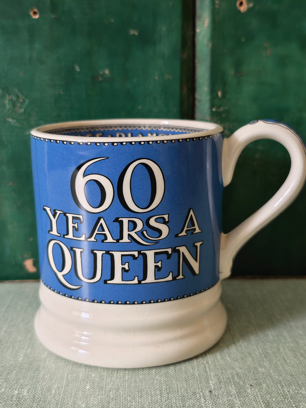 A ceramic mug with a blue and white design celebrating '60 Years A Queen' in bold white lettering
