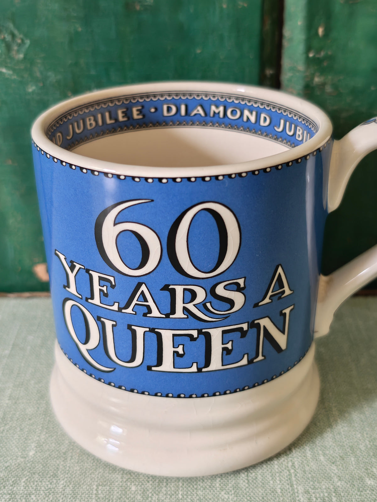 A ceramic mug with a blue and white design celebrating '60 Years A Queen' in bold white lettering