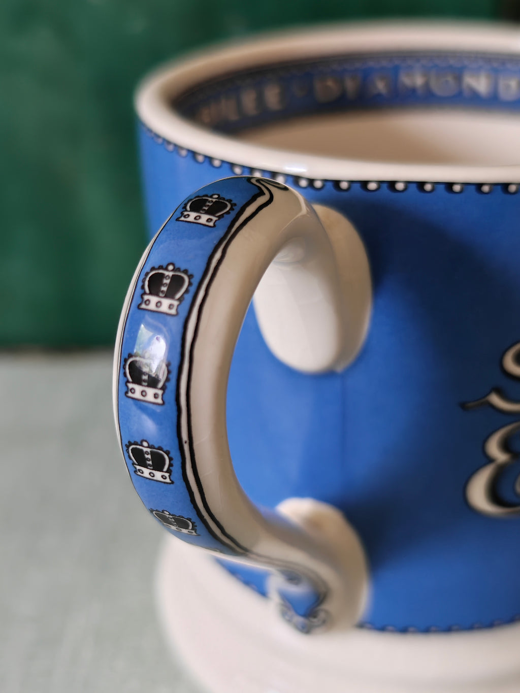 Close-up of a blue ceramic mug with a white handle, decorated with black crown motifs and white script lettering.