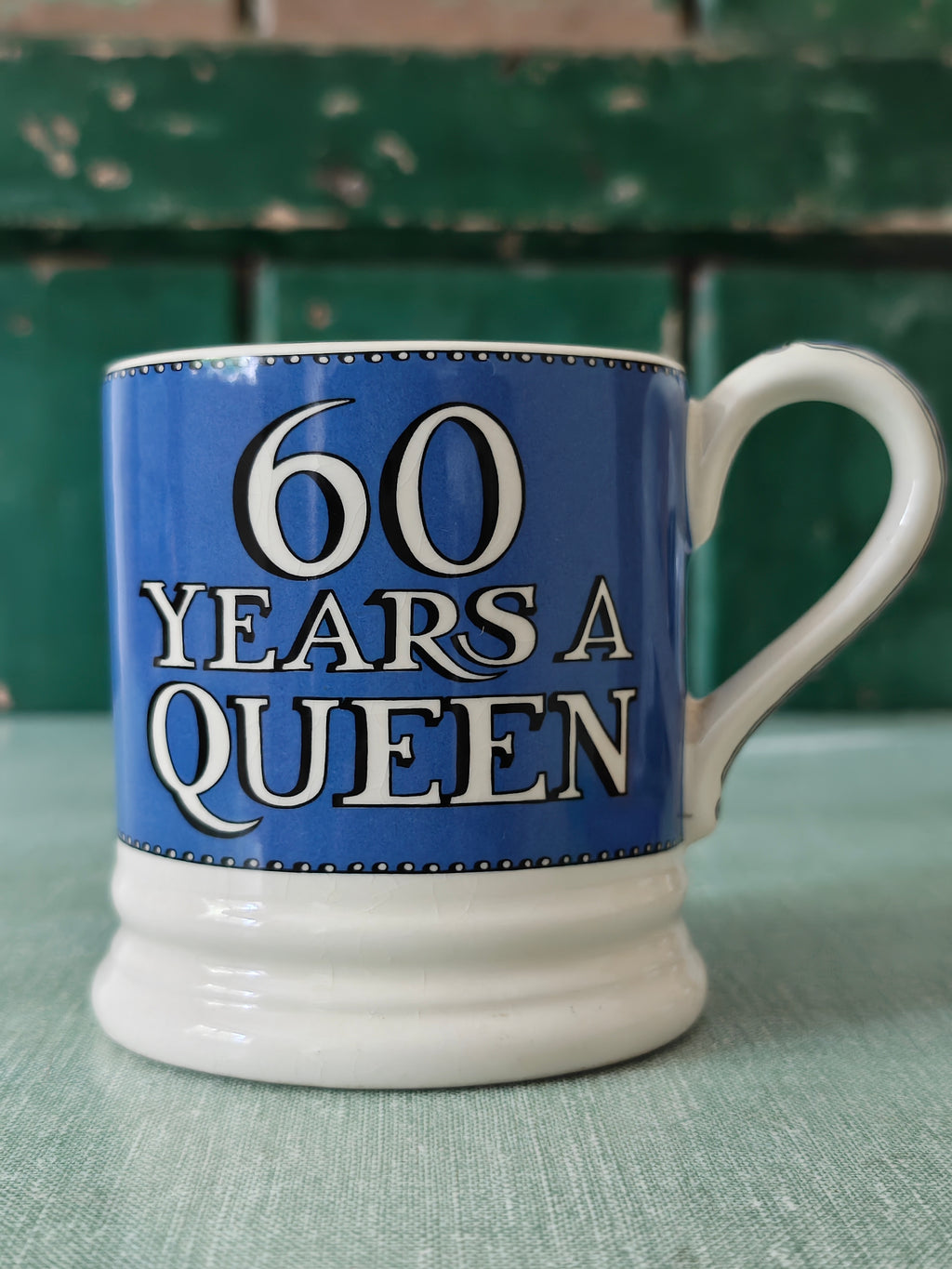 A ceramic mug with a blue and white design celebrating '60 Years A Queen' in bold white lettering