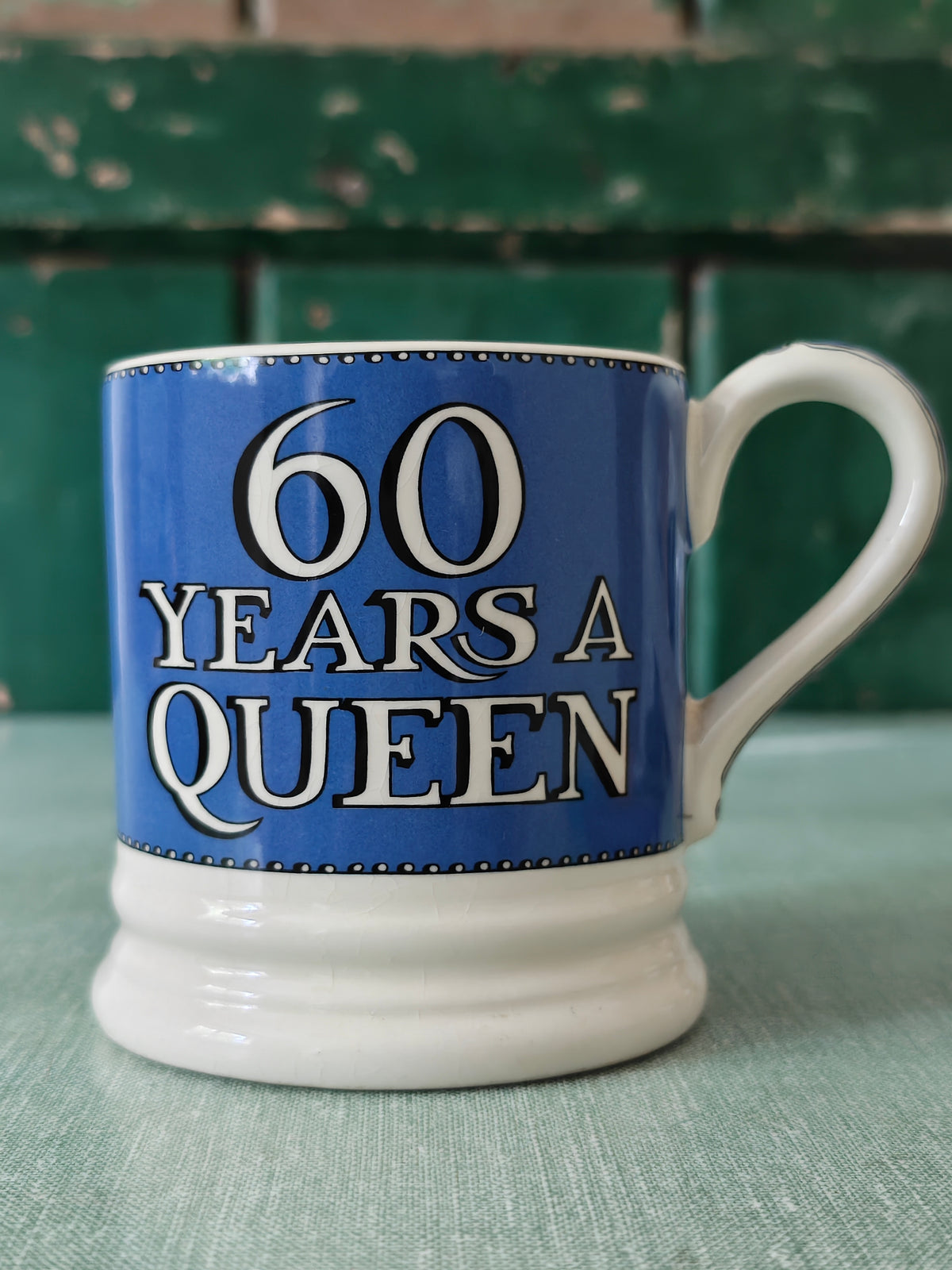 A ceramic mug with a blue and white design celebrating '60 Years A Queen' in bold white lettering