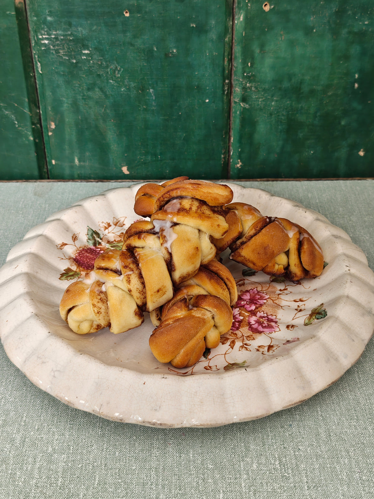 Cinnamon rolls topped with white icing, served on a white ceramic plate with a floral pattern