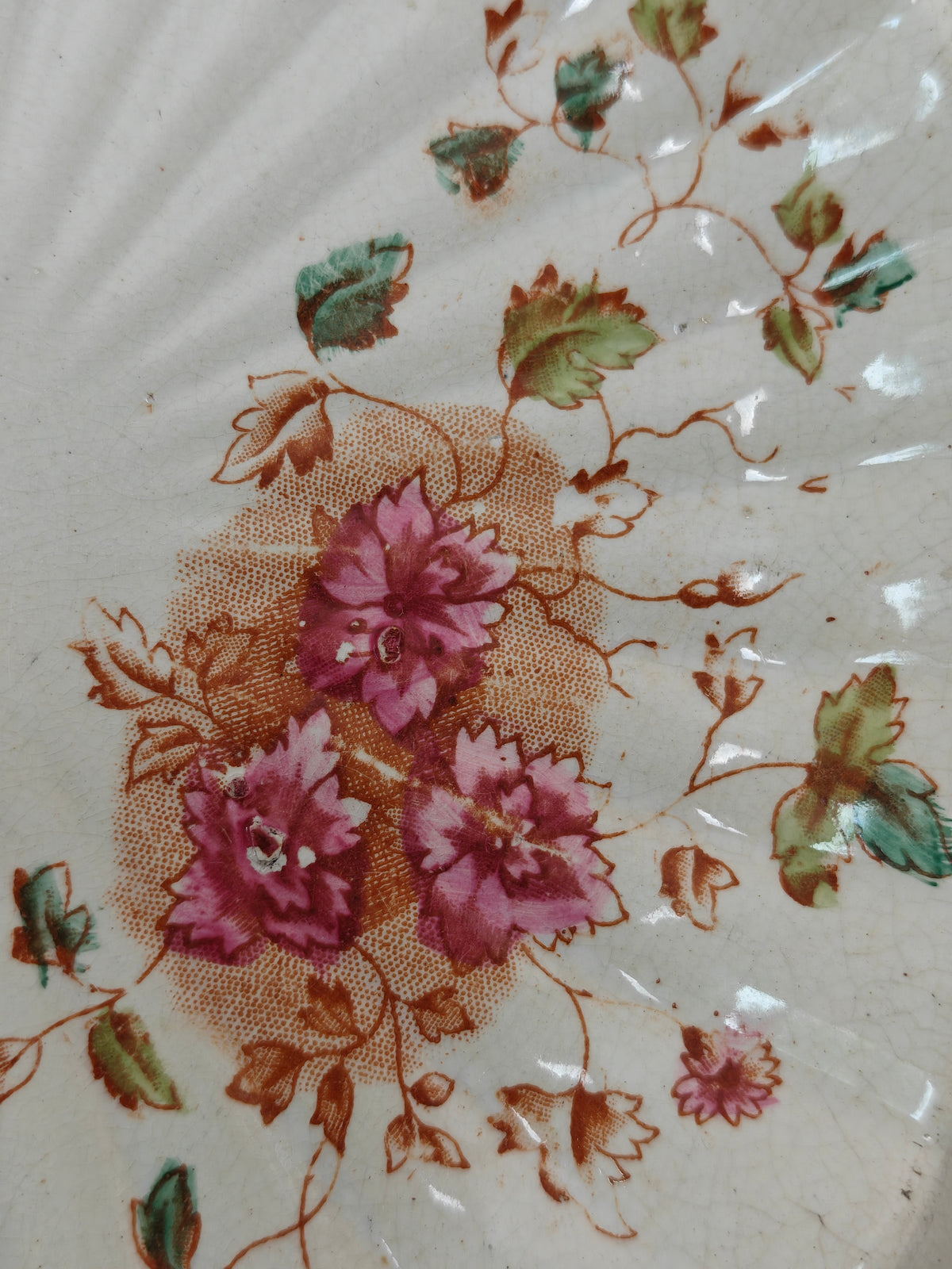 Close-up of a vintage ceramic plate or dish featuring a floral pattern with pink flowers and green leaves on a cream-colored background.
