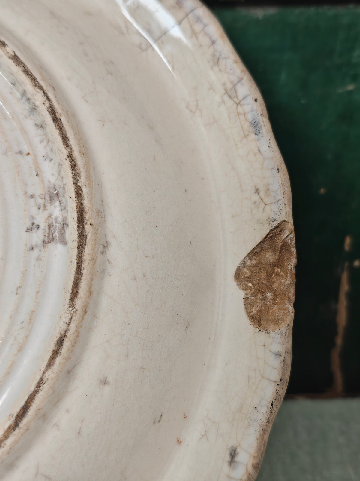 Close-up of a vintage off-white ceramic plate with a scalloped rim, showing a prominent brown chip on the edge.