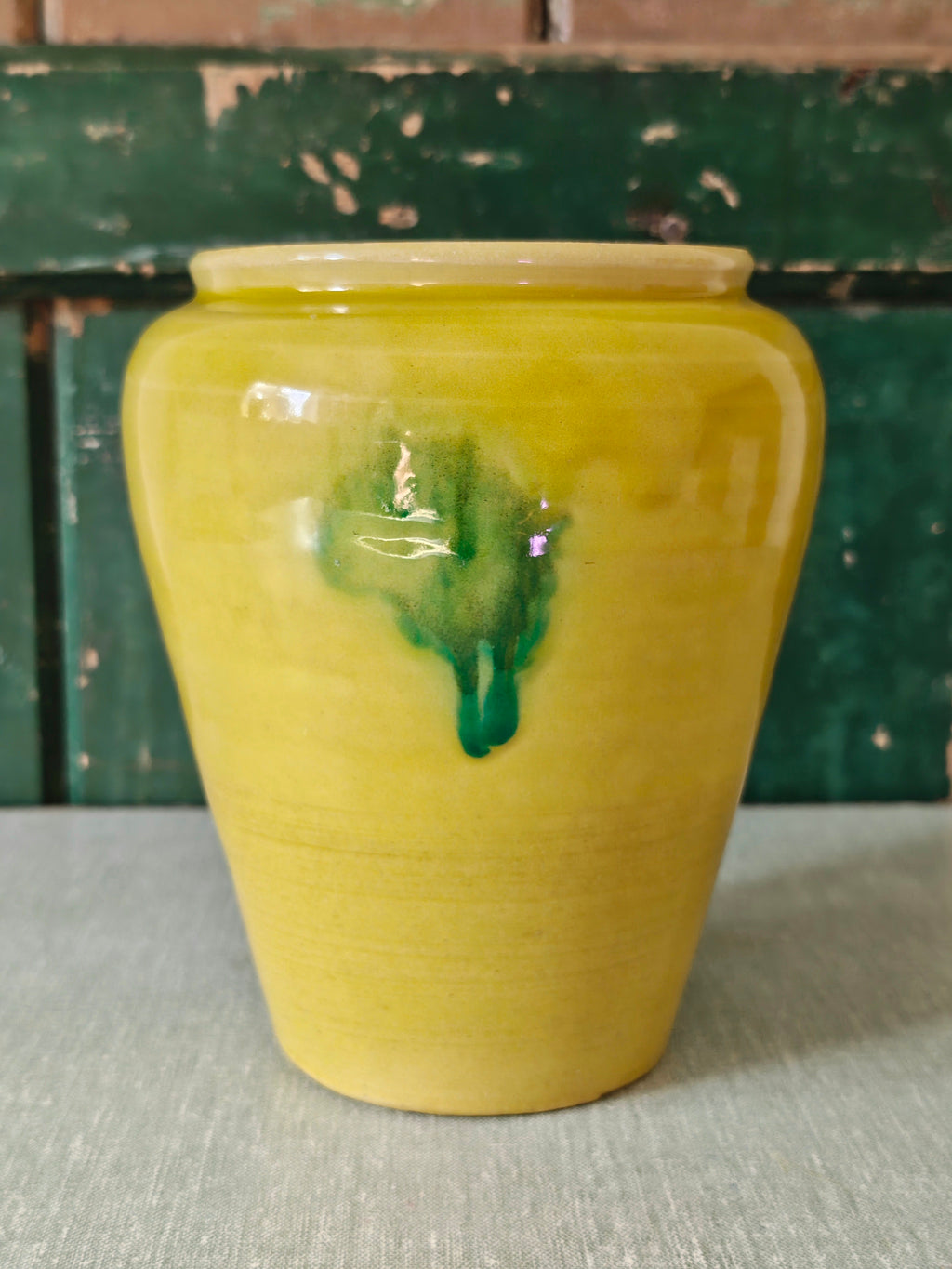 A yellow glazed ceramic jar with a green drip glaze design