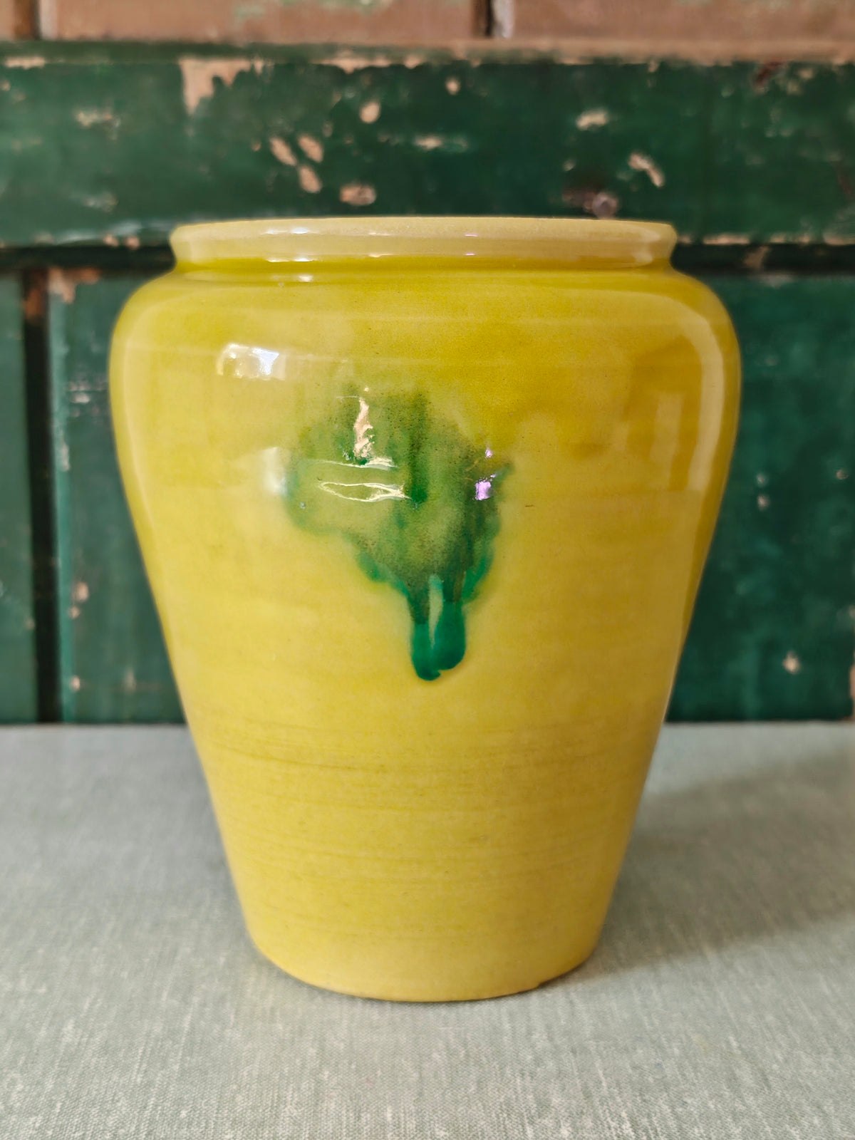 A yellow glazed ceramic jar with a green drip glaze design