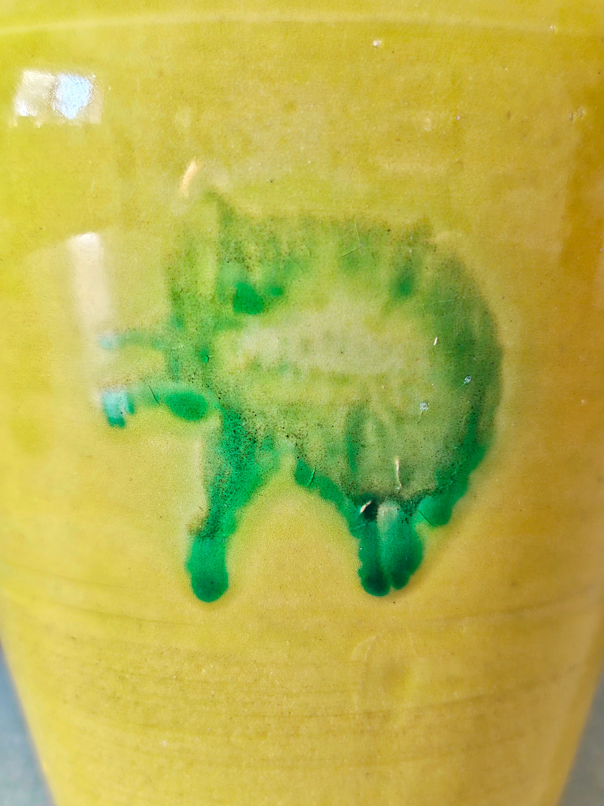 Close-up of yellow glazed ceramic jar with a green drip glaze design