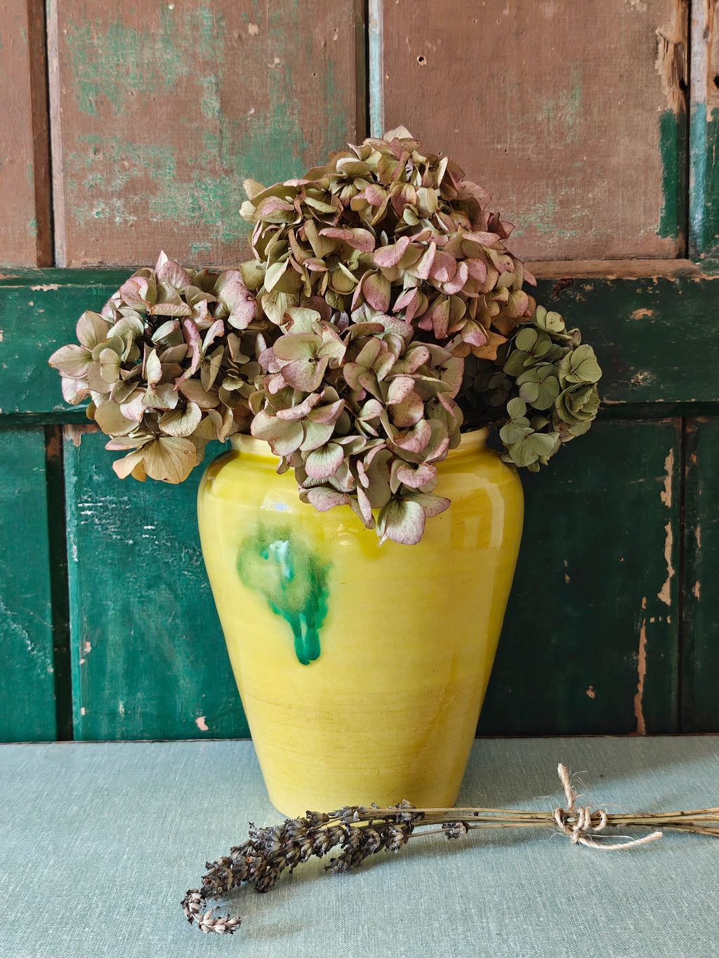 A yellow glazed ceramic jar with a green drip glaze design displayed with flowers