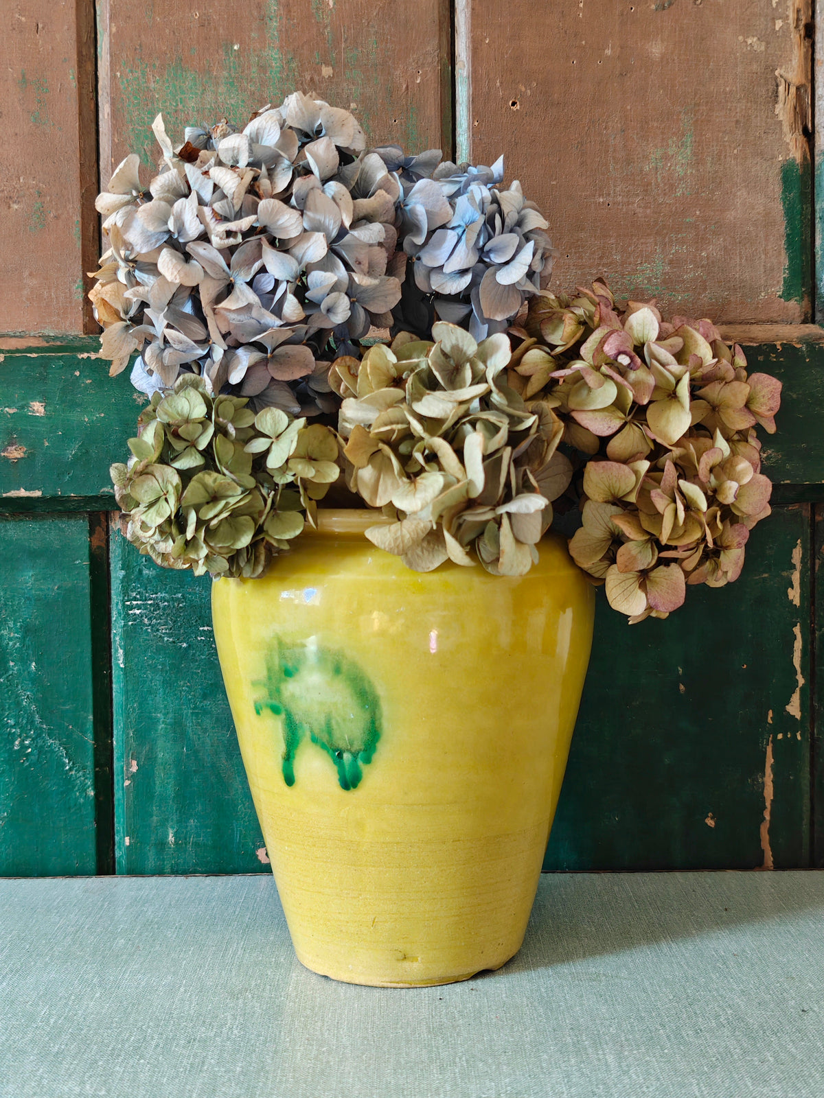 A yellow glazed ceramic jar with a green drip glaze design, displayed with flowers