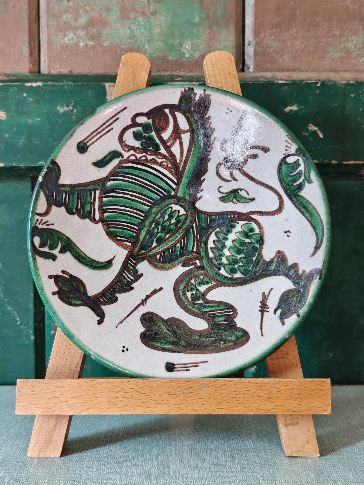 A round ceramic plate with a hand-painted green and brown dragon design on a white background.