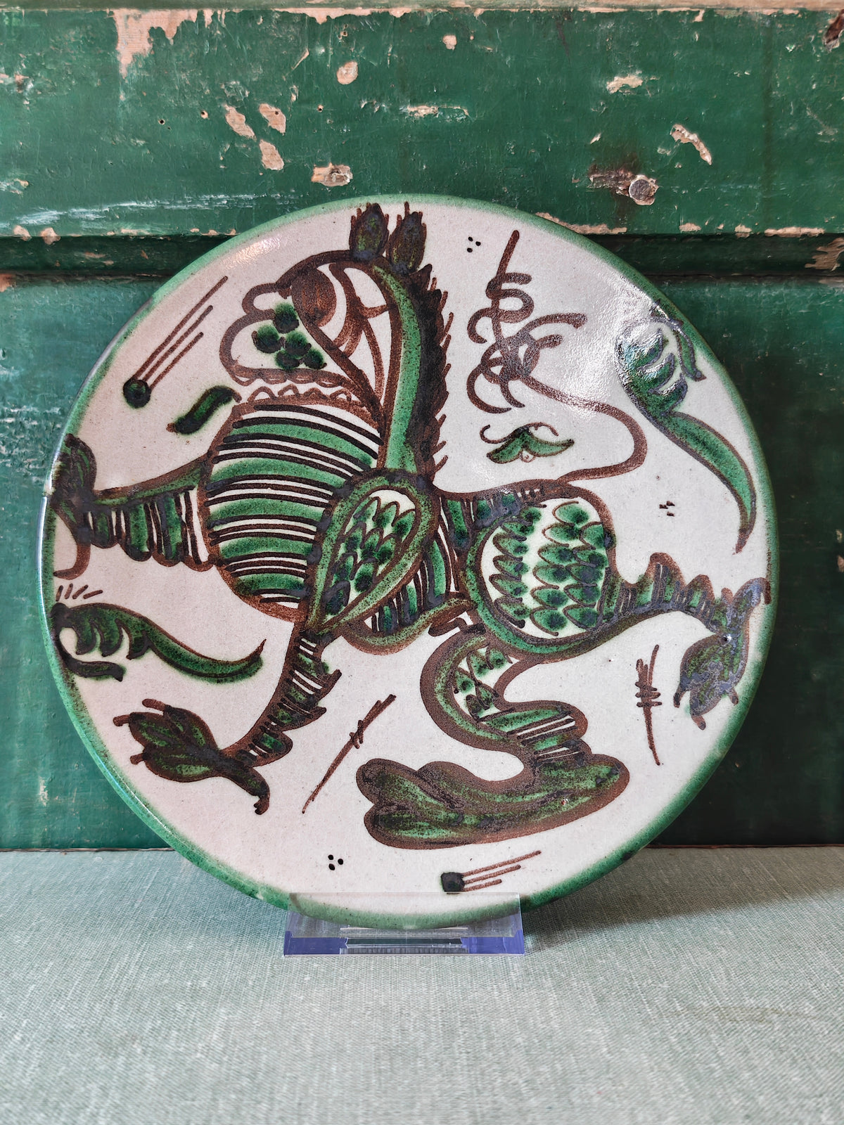 A round ceramic plate with a hand-painted green and brown dragon design on a white background.
