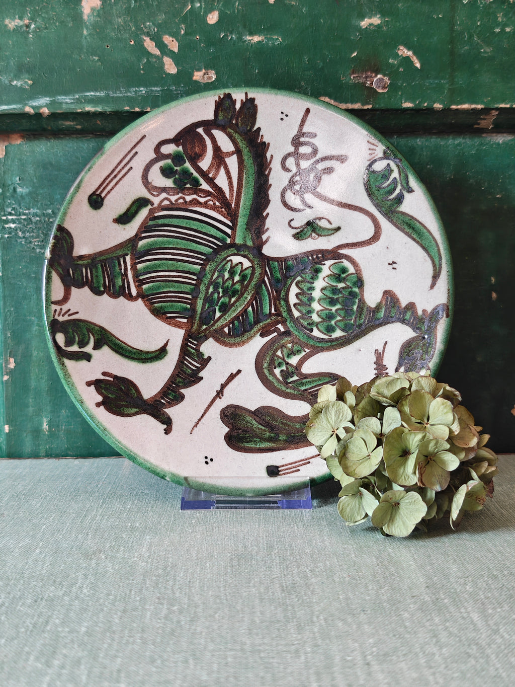 A round ceramic plate with a hand-painted green and brown dragon design on a white background.