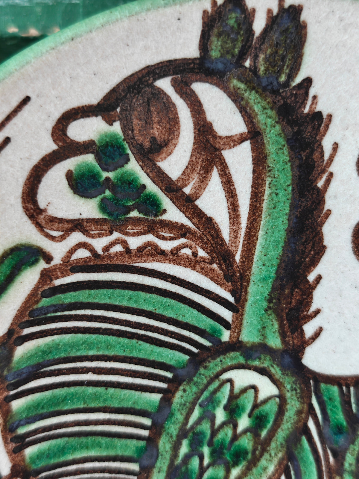 Close up of the head of a hand painted dragon design on a round ceramic plate.