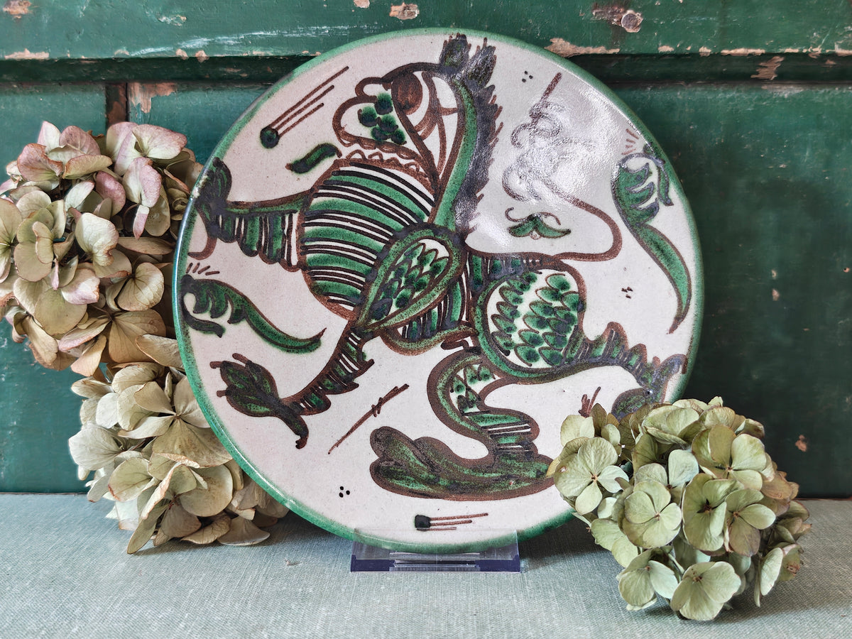 A round ceramic plate with a hand-painted green and brown dragon design on a white background.