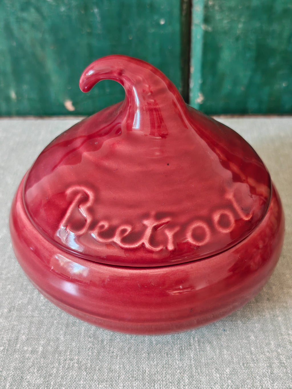 A glossy red ceramic lidded jar with a sculpted lid resembling a beetroot and embossed text.