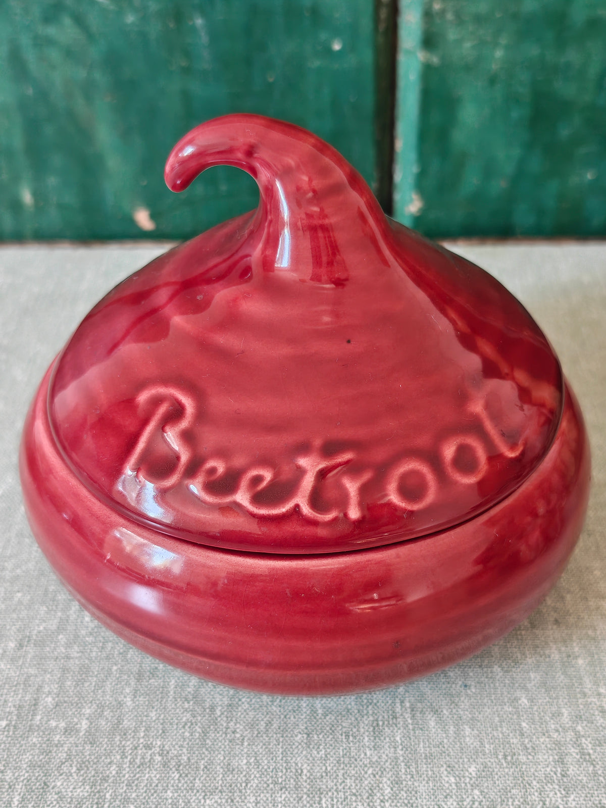 A glossy red ceramic lidded jar with a sculpted lid resembling a beetroot and embossed text.