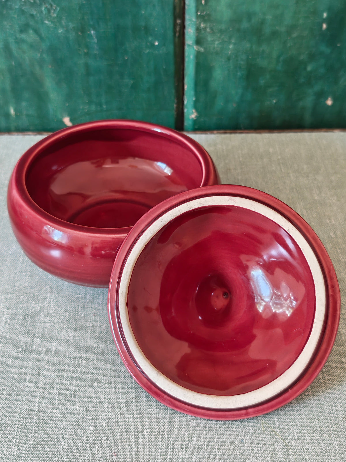 A glossy deep red ceramic bowl with its matching lid placed in front.