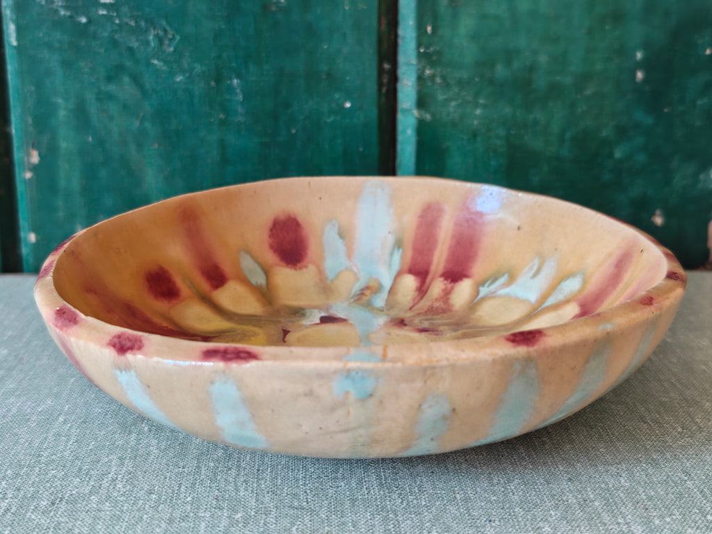 A handmade ceramic bowl with a beige glaze and abstract drip glaze pattern in blue, red and gold.