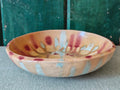 A handmade ceramic bowl with a beige glaze and abstract drip glaze pattern in blue, red and gold.