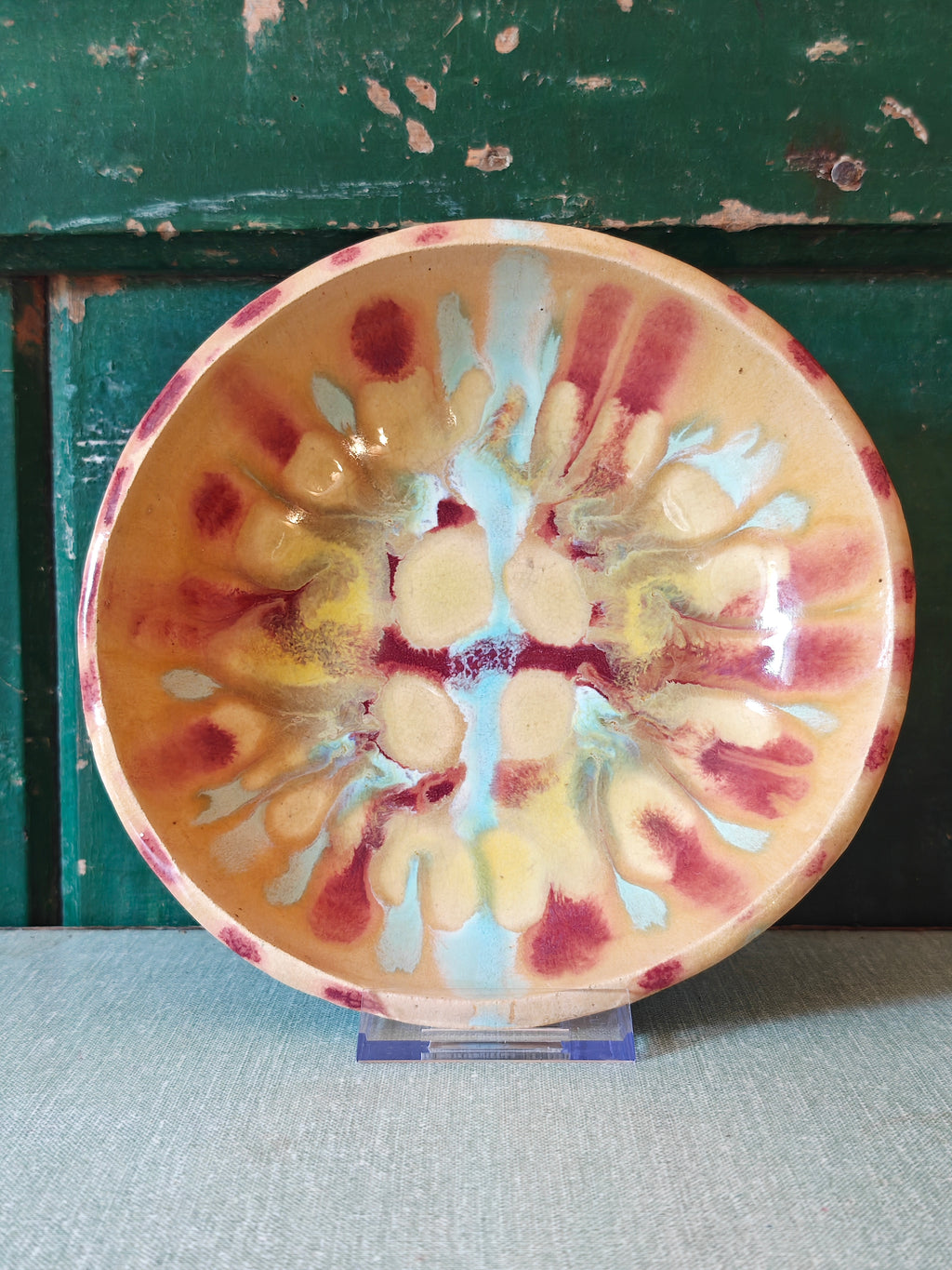A handmade ceramic bowl with a beige glaze and abstract drip glaze pattern in blue, red and gold.