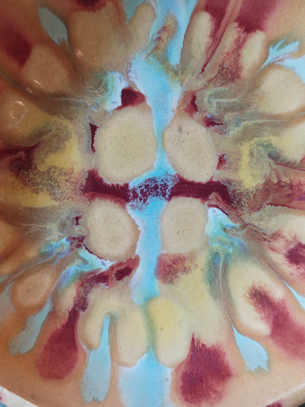 Close up the inside of a handmade ceramic bowl with a beige glaze and abstract drip glaze pattern in blue, red and gold.