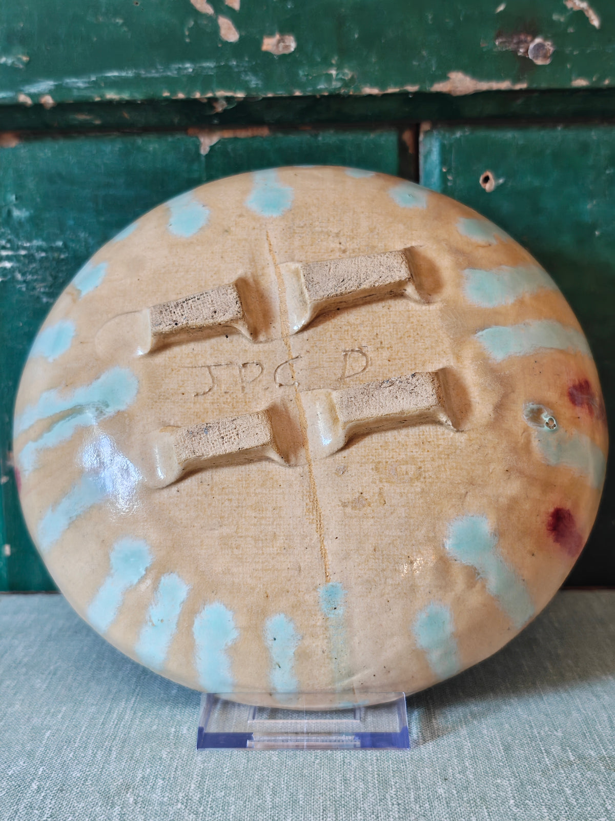 Underside of a handmade ceramic bowl showing blue drip glaze and pedestal feet with the makers intials