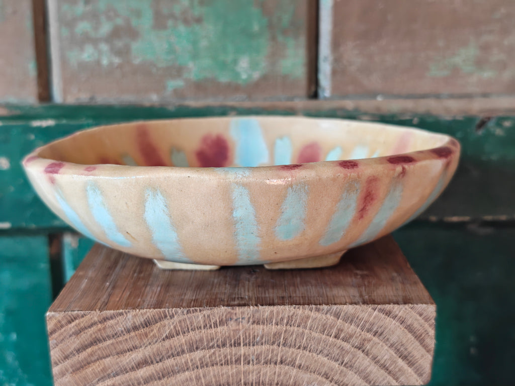 Side view of a handmade ceramic bowl with a beige glaze and abstract drip glaze pattern in blue, red and gold.
