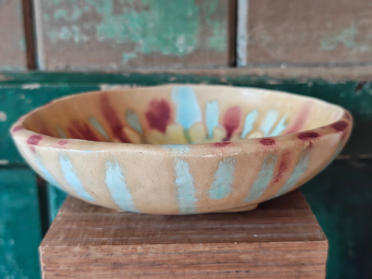 A handmade ceramic bowl with a beige glaze and abstract drip glaze pattern in blue, red and gold.