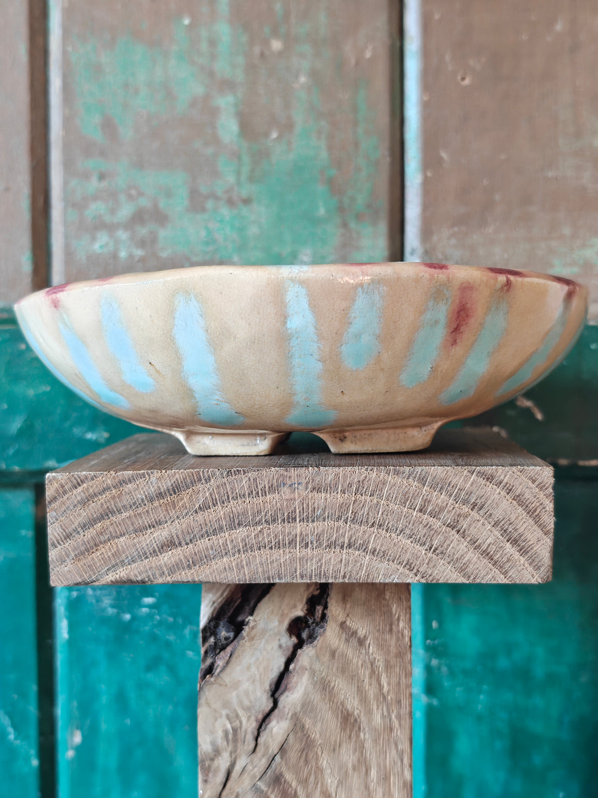 Side view of a handmade ceramic bowl with a beige glaze and abstract drip glaze pattern in blue, red and gold.