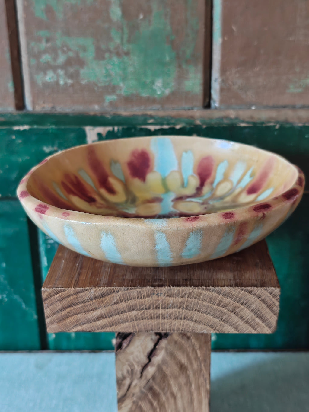 A handmade ceramic bowl with a beige glaze and abstract drip glaze pattern in blue, red and gold.