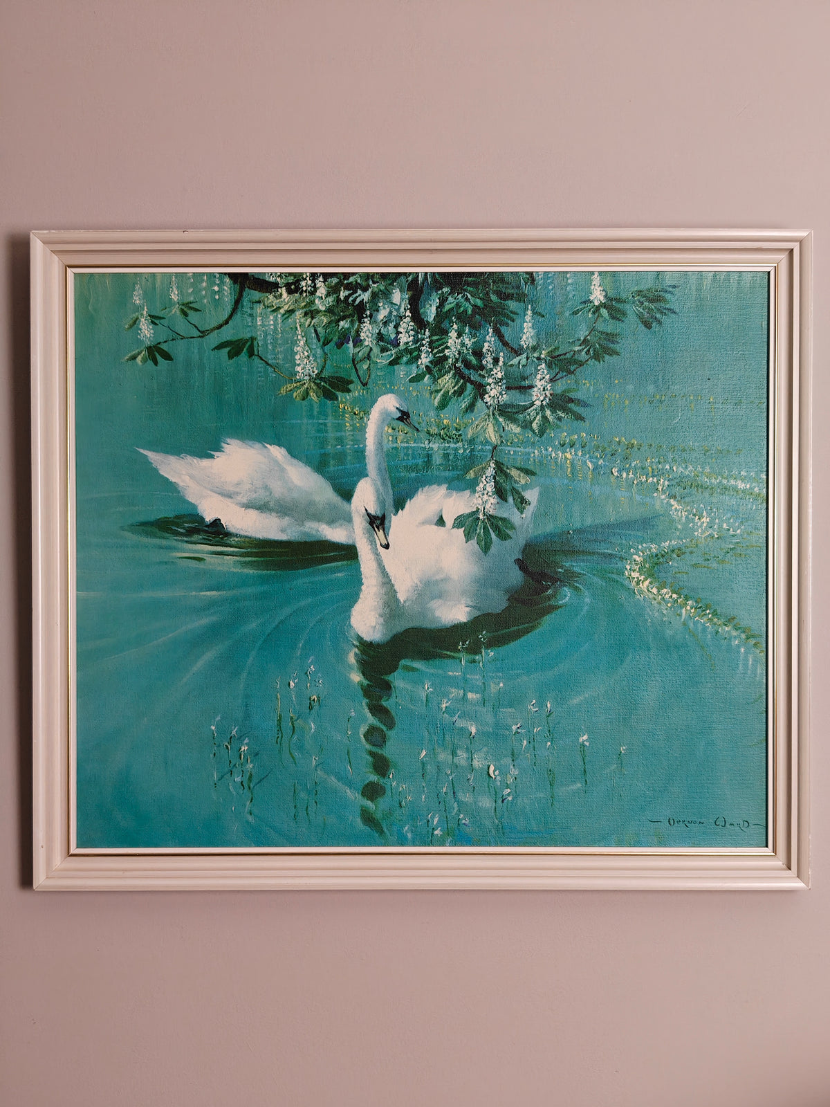 A framed painting of two white swans on a turquoise lake under hanging green leaves.
