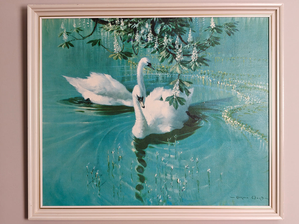 A framed painting of two white swans swimming in a turquoise pond under hanging white flowers, set in a white frame.